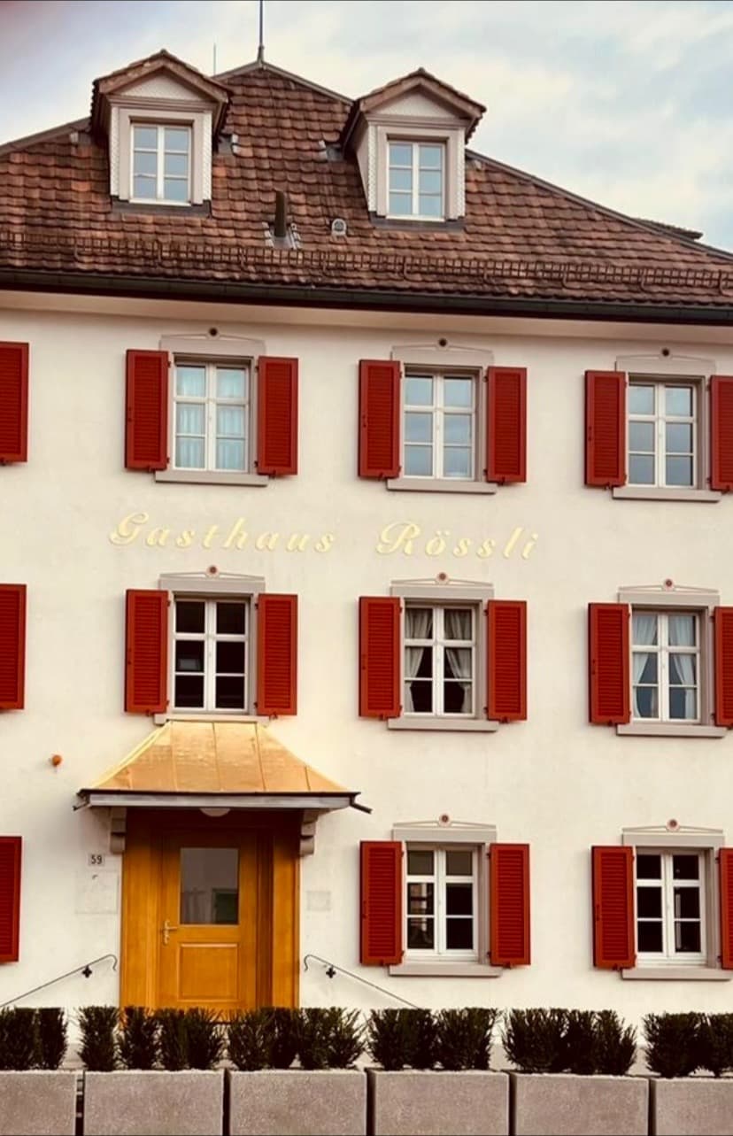 Weisse Fassade des Gasthauses Rössli in Wil mit roten Fensterläden, goldenem Schriftzug und goldenem Vordach