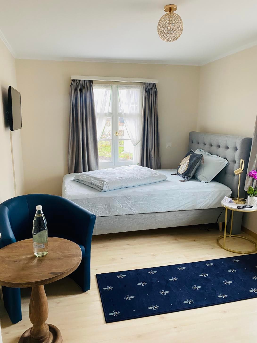 Zimmer mit grauem Polsterbett, Orchidee und blauem Teppich im Gasthaus Rössli Wil